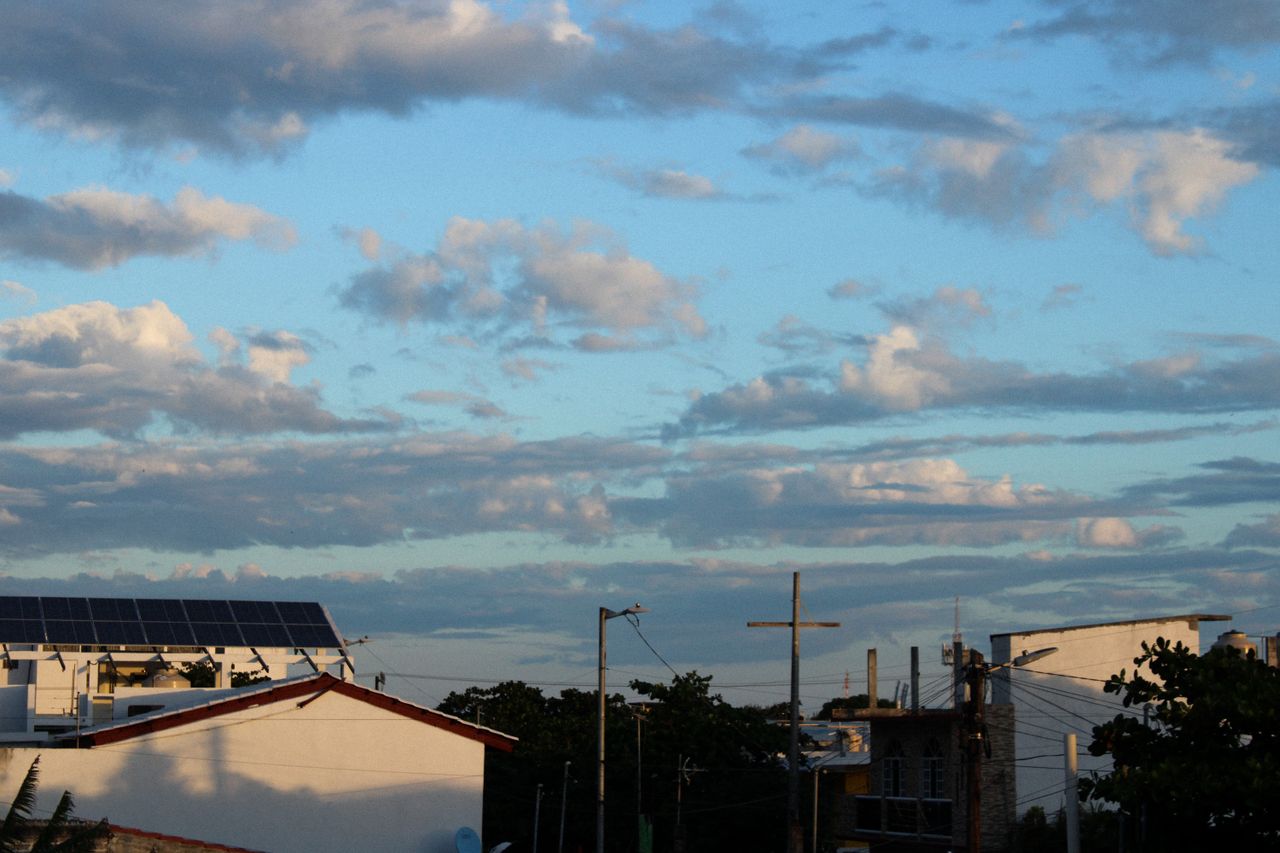 why-choose-us A scenic view of rooftops with solar panels under a cloudy blue sky during the day.